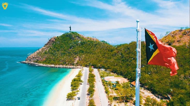 The Cristo Rei statue above the white beach at Dili, with the Timor-Leste flag flying.